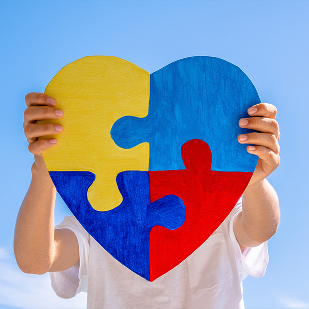 Dłonie chłopca trzymające kolorowe puzzle w kształcie serca na tle błękitnego nieba. Światowy Dzień Świadomości Autyzmu, koncepcja zaburzeń ze spektrum autyzmu.